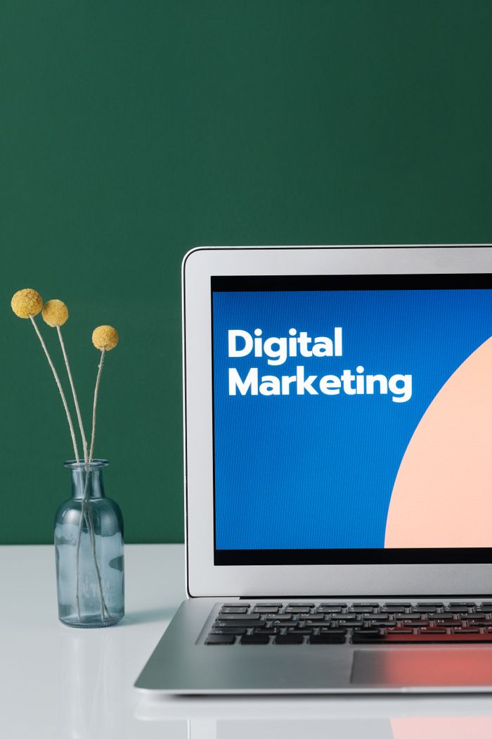 stats-img A laptop displaying 'Digital Marketing' with a minimalist floral decor in a glass vase.